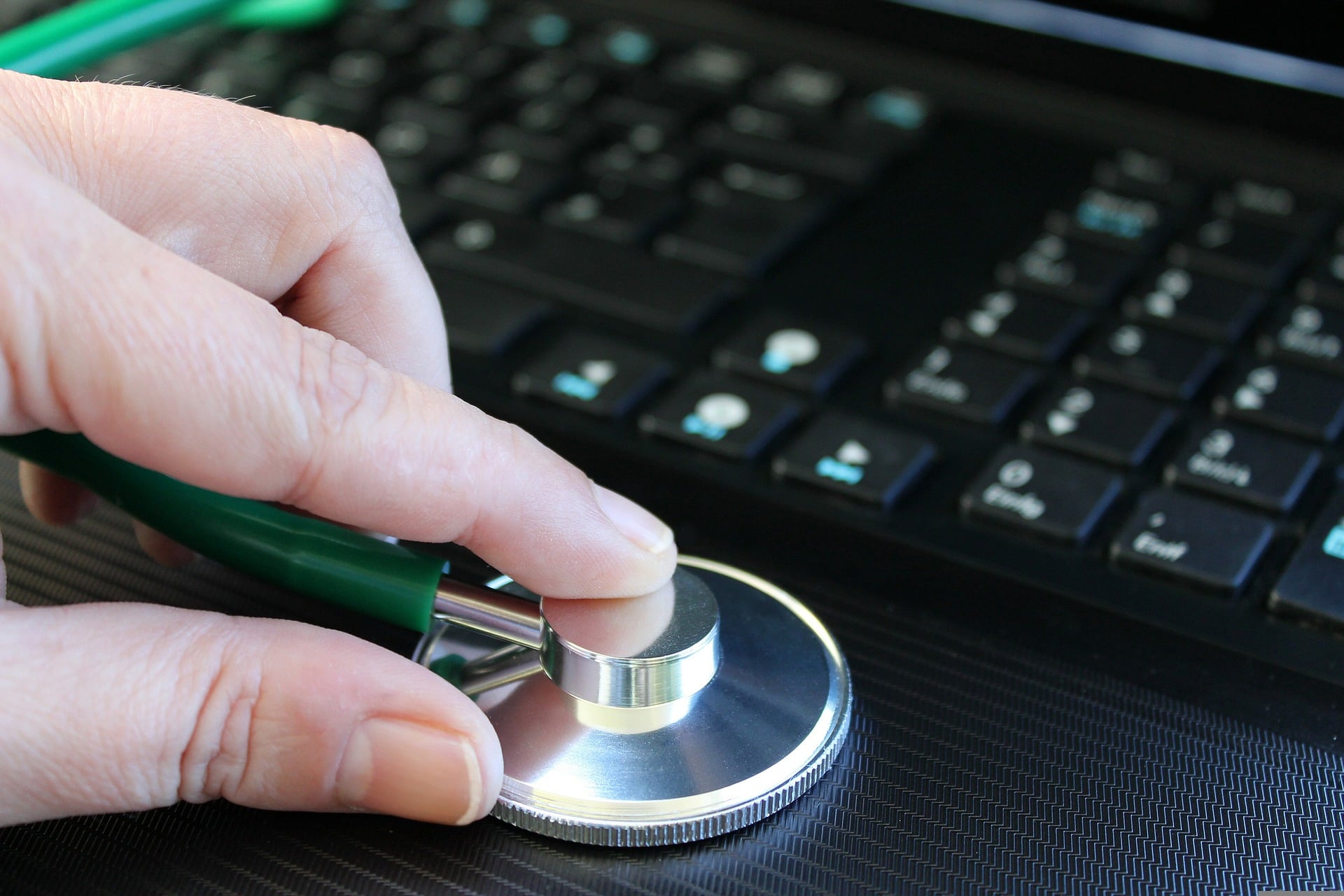 A hand holding the end of a stethoscope in front of a computer keyboard